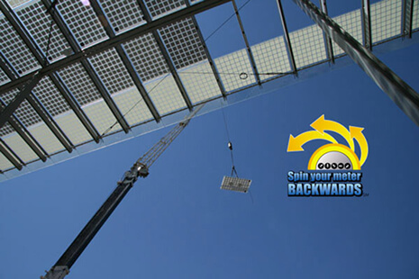 Crane lifts a panel under a metal framework against a blue sky, with a 'Spin your meter BACKWARDS' graphic in the corner.