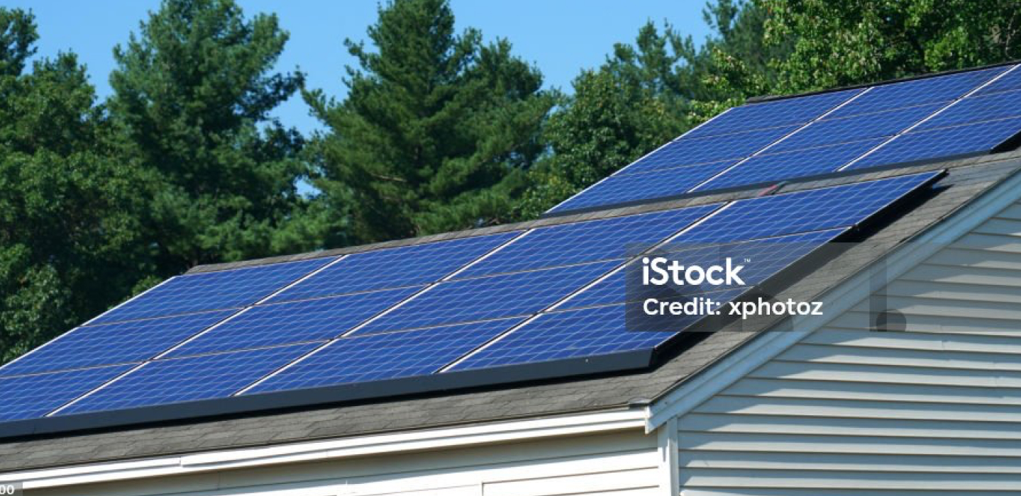Residential roof with blue solar panels installed, greenery in the background under a clear sky.
